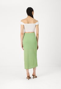 Balta off-the-shoulder top un griezuma košā, garš pieguļošs zaļš svārks ar gludu tekstūru, valkāts ar brūnām papēžu mūlēm.
