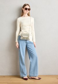 Cream long-sleeve top, light blue wide-leg jeans, maroon open-toed flats, and a shiny silver bag with a crystal accent. Brown square sunglasses.