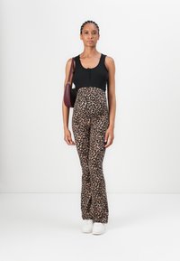 Débardeur noir à côtes avec détail de boutonnage ; pantalon évasé imprimé léopard ; modèle portant des baskets blanches et tenant un sac à main bordeaux.