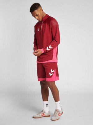 Bordeaux atletiek trainingspak met een top met kwart rits. De top heeft witte accenten en roze mouwen. Inclusief bordeaux korte broek met roze rand en wit logo.