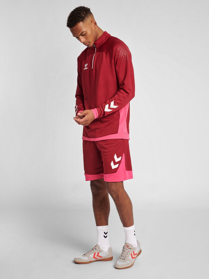 Kastanjebrun atletisk träningsoverall med kvartdragkedja. Överdelen har vita detaljer och rosa ärmar. Inkluderar kastanjebrun shorts med rosa kontraster och vit logotyp.