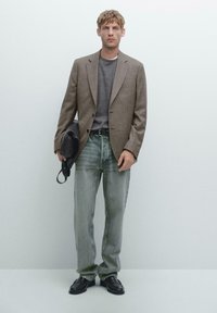 Brown plaid blazer, grey crew-neck sweater, light-wash distressed jeans, black belt, black loafers, holding a black leather shoulder bag.