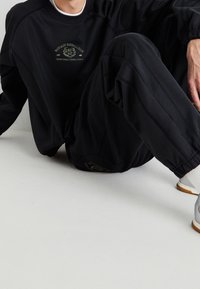 Czarna bluza i spodnie z logo "Fantazy Fussball Club" w kolorze złotym. Miękki materiał, luźny krój i elastyczne mankiety.