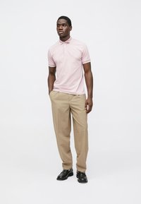 Polo rosa claro com gola e mangas curtas, combinada com calças bege. O conjunto apresenta um ajuste personalizado e textura suave.