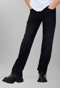 Jeans de mezclilla negra con corte recto, con costuras sutiles, bolsillos delanteros y combinados con botas negras gruesas hasta el tobillo.