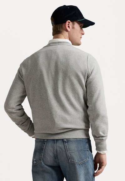 Gray cotton sweatshirt with a round neckline and long sleeves, paired with blue denim jeans. The person wears a navy cap with a green accent.