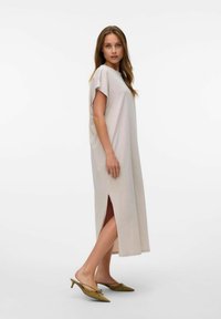 Jasno beżowa sukienka maxi z krótkimi rękawami i bocznymi rozcięciami. Gładki materiał i luźny krój. W zestawieniu z oliwkowozielonymi butami typu slingback z ostrym noskiem.