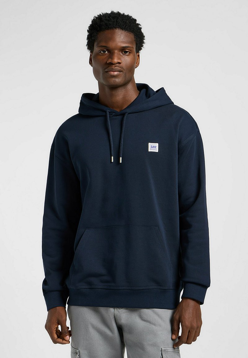 Sudadera azul marino de tela suave, que cuenta con un bolsillo tipo canguro, capucha con cordón y un pequeño parche con el logo en el pecho.