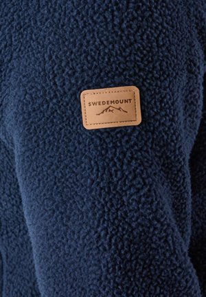 Navy blue fleece jacket with a textured surface. Features a tan leather patch labeled "SWEDEMOUNT" with mountain graphic.