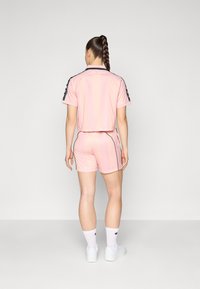 Conjunto atlético rosa composto por um top curto de mangas curtas e calções combinantes. O design inclui detalhes em preto e riscas laterais.