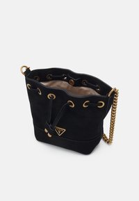 Bolso tipo cubo de ante negro con herrajes dorados, que incluye una correa de cadena, cierre con cordón y una placa con el logo en la parte frontal.