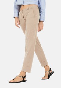 Beige tapse broeken met zijzakken, van gladde stof en voorzien van een omslag. Gecombineerd met zwarte platte sandalen versierd met embellishments.