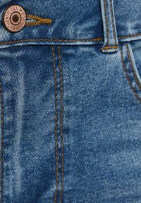 Primer plano de jeans de mezclilla azul que muestran botón de cobre, costuras naranjas y área del bolsillo delantero.