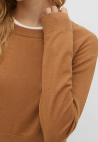 Suéter de punto marrón con cuello redondo y cuello interior blanco, con mangas largas y puños acanalados, textura suave.
