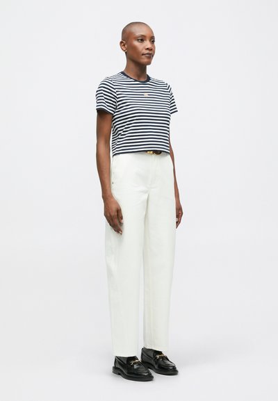Prúhované námornícke a biele skrátené tričko, voľný strih, spárované s bielymi nohavicami s vysokým pásom a čiernymi topánkami so zlatými akcentami.