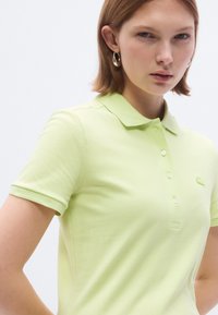 Polo vert clair avec un col, manches courtes et quatre boutons. Présente un petit logo brodé sur la poitrine.