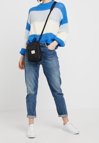 Niebiesko-biały sweter w paski o luźnym kroju, zestawiony z jasnoniebieskimi podwiniętymi dżinsami i białymi trampkami. Czarna torebka na ramię przewieszona przez ciało.