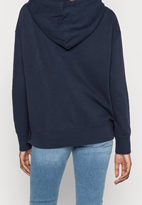 Mörkblå huvtröja med dragsko, långa ärmar och avslappnad passform. Tillverkad av mjukt tyg med en enkel design och ribbade muddar.