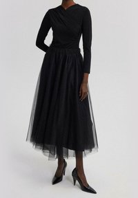 Zwarte lange mouwen jurk met kruisbodice, elastische tailleband en een gelaagde tule rok. Afgewerkt met strakke zwarte hoge hakken.