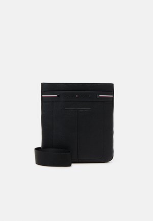 Schwarze Leder-Crossbody-Tasche mit strukturierter Oberfläche, ausgestattet mit einem Logo auf der Vorderseite und einem abnehmbaren Stoffriemen. Minimalistisches Design mit dezenten Akzenten.
