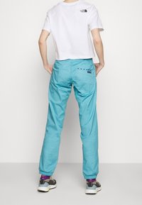 Person wearing a white cropped North Face t-shirt, light blue jogger pants with elastic cuffs and back pocket, and multicolor sneakers standing facing backward.