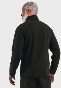 Schwarze gestepptes Fleecejacke mit hohem Kragen, langen Ärmeln und strukturiertem Stoff. Hat eine lockere Passform und ein minimalistisches Design.