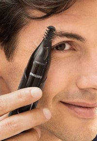 Philips grooming trimmer, black, with a tapered design and washable feature, used for shaping eyebrows with fine bristle-like trimming head.