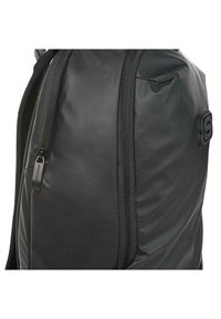 Mochila negra con una textura suave y mate, compartimentos con cremallera y un logo destacado, fabricada con un tejido duradero y costuras reforzadas.