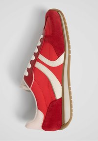 Chaussure de sport rouge combinant des matériaux en daim et synthétiques, avec des accents blancs, une semelle intermédiaire texturée et une semelle extérieure en caoutchouc.