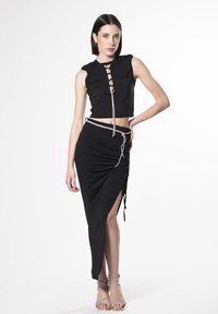 Top corto negro sin mangas con frente de cordones, combinado con una falda larga negra con una abertura lateral y un acento atado. Tacones plateados con tiras.