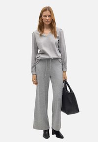 Sudadera gris con escote en V y mangas largas, combinada con pantalones de chándal de pierna ancha a juego. Presenta un cinturón ajustable y un bolso negro.