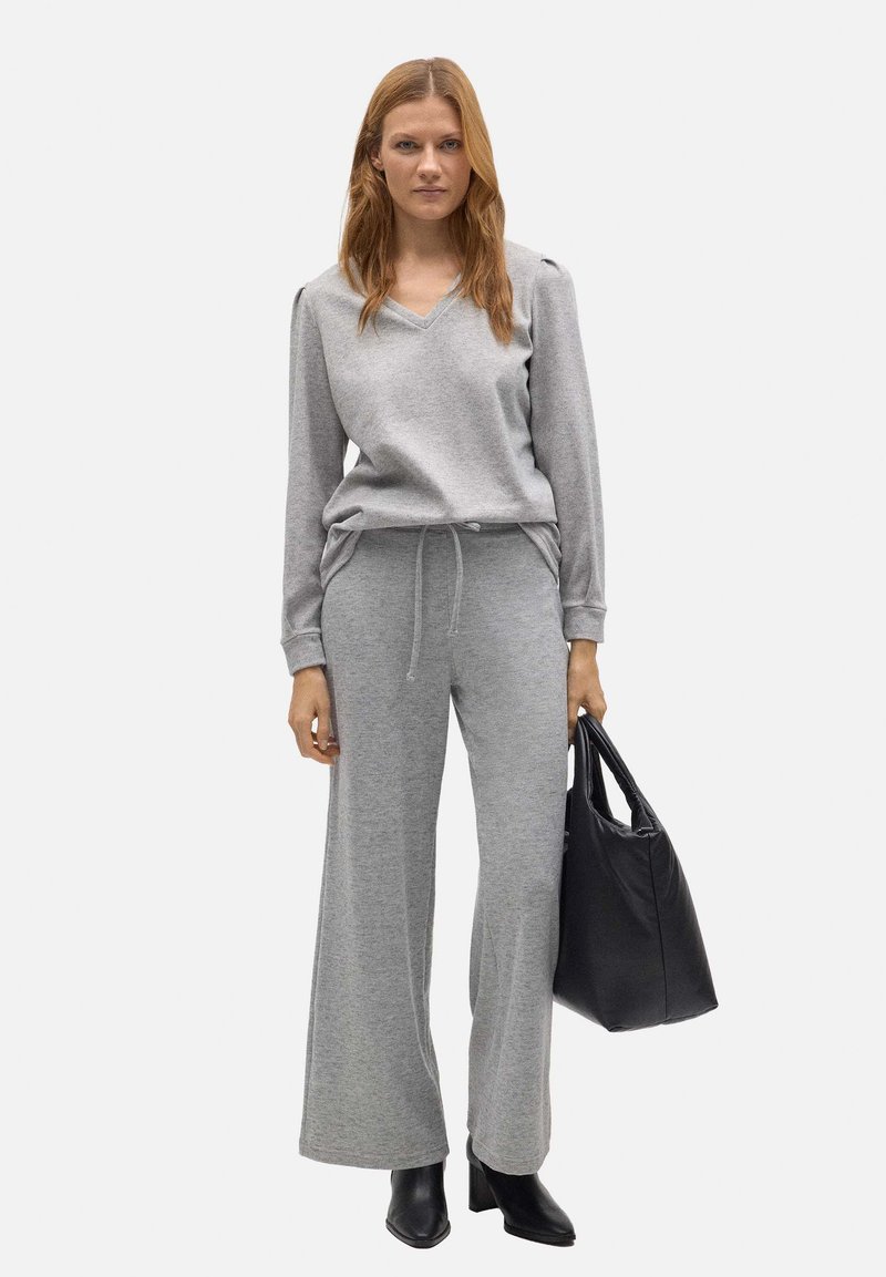 Sudadera gris con escote en V y mangas largas, combinada con pantalones de chándal de pierna ancha a juego. Presenta un cinturón ajustable y un bolso negro.