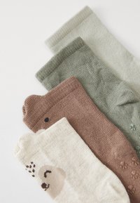 Vier Paar Socken in verschiedenen Farben: cremefarben mit einem Bärenmotiv, hellbraun, olivgrün und strukturisiertem Grau; alle sind aus geripptem Strick.