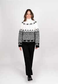 Knitted black and white sweater with a high collar, featuring geometric patterns, and contrasting textured designs; paired with black pants.
