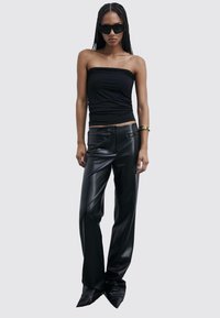 Top nero senza spalline abbinato a pantaloni neri in ecopelle con silhouette aderente e texture lucida, completato da scarpe nere a punta.