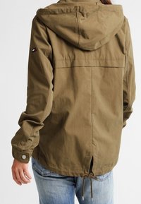 Olivgrön huvjacka i lätt tyg, med dragsko i midjan och tryckknappar vid ärmsluten. Baksidan har en enkel design.