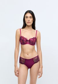 Conjunto de sujetador y braguitas de encaje en burdeos oscuro, con patrones florales y acentos transparentes, con tirantes ajustables y un detalle de ojal en la parte frontal.