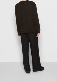 Schwarzer Sweatshirt mit entspannter Passform, gerippten Bündchen und Saum. Kombiniert mit lockeren schwarzen Hosen und flachen Schuhen, ohne sichtbare Muster oder Akzente.