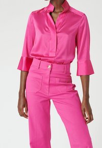Blouse en satin rose vif avec col et manches trois-quarts, associée à un pantalon rose vif taille haute avec poches et bouton.