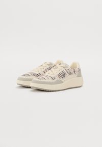 Beige sneakers met een gestructureerde breisel bovenkant met meerkleurige strepen, lichtgrijze accenten, en een geribbelde rubberen zool.