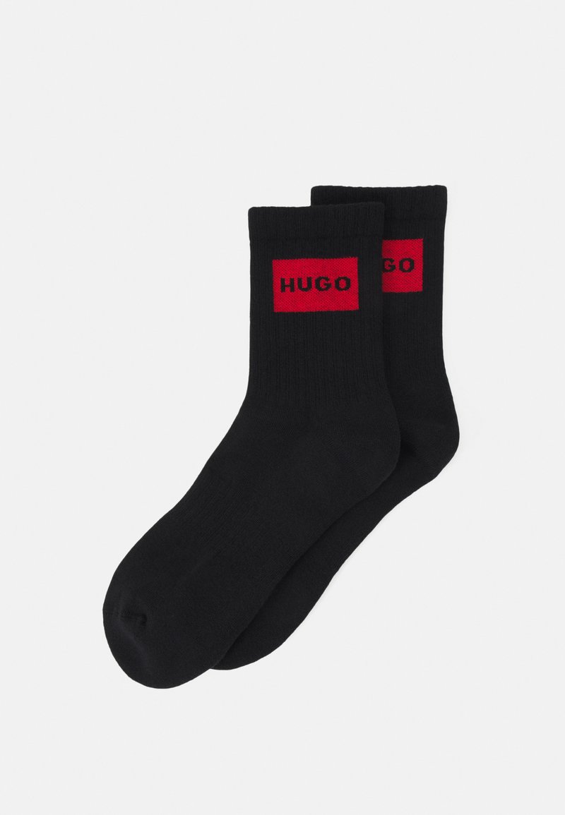 Crne čarape s rebrastom teksturom, s crvenim pravokutnim logotipom na gornjoj strani na kojem je istaknuto ime "HUGO".