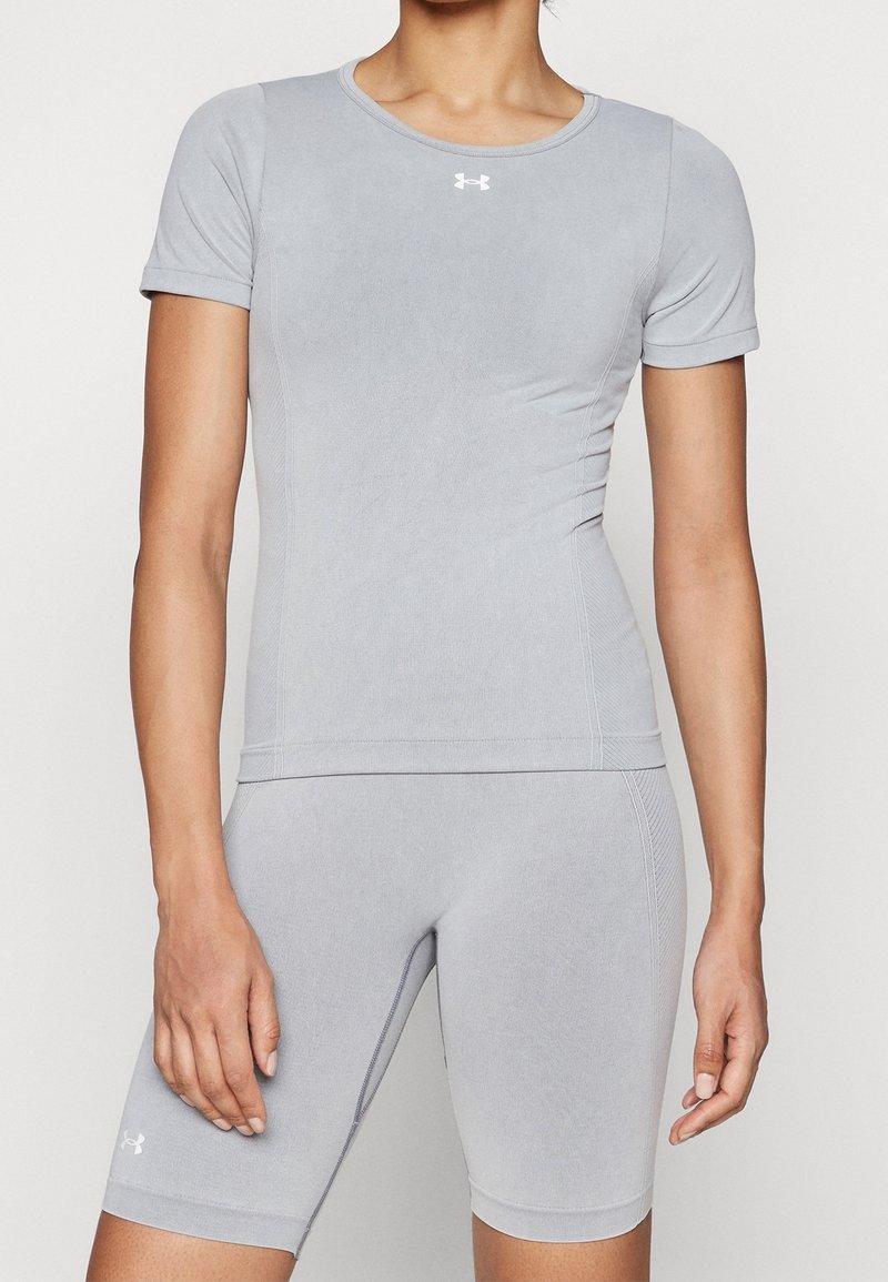 Femme portant un haut ajusté gris clair à manches courtes et un short de sport assorti à mi-cuisse avec de petits logos blancs.