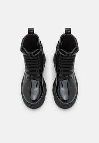 Zwarte enkellaarzen met een glanzende lakafwerking, contrasterende gestructureerde veters en een dikke zwarte zool. Voorzien van een lus aan de achterkant voor eenvoudig aan- en uittrekken.