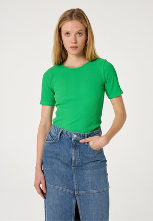 Grove groene top met ribbels en korte mouwen, gecombineerd met een blauwe denim rok met een voorkantsplits en zichtbare knoopdetails. Strak ontwerp en textuur.