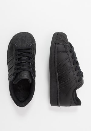 Paire de baskets basses noires avec un design bout coquille et des lacets, montrée en vues de dessus et de côté sur fond blanc.