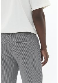 Pantaloni cu carouri în alb și negru, cu o croială slim, dotati cu un brâu solid și două buzunare la spate. Realizați dintr-un materialtexturat.