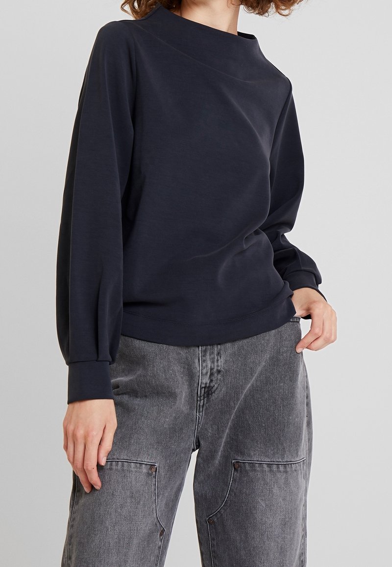 Pullover blu navy con colletto alto, vestibilità morbida e maniche a palloncino. Realizzato in materiale morbido, con superficie testurizzata e polsini a coste.