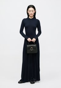 Granatowa sukienka z długim rękawem z guzikami na rękawach, zestawiona z małą czarną torebką z okrągłym uchwytem. Gładki, fakturowany materiał.