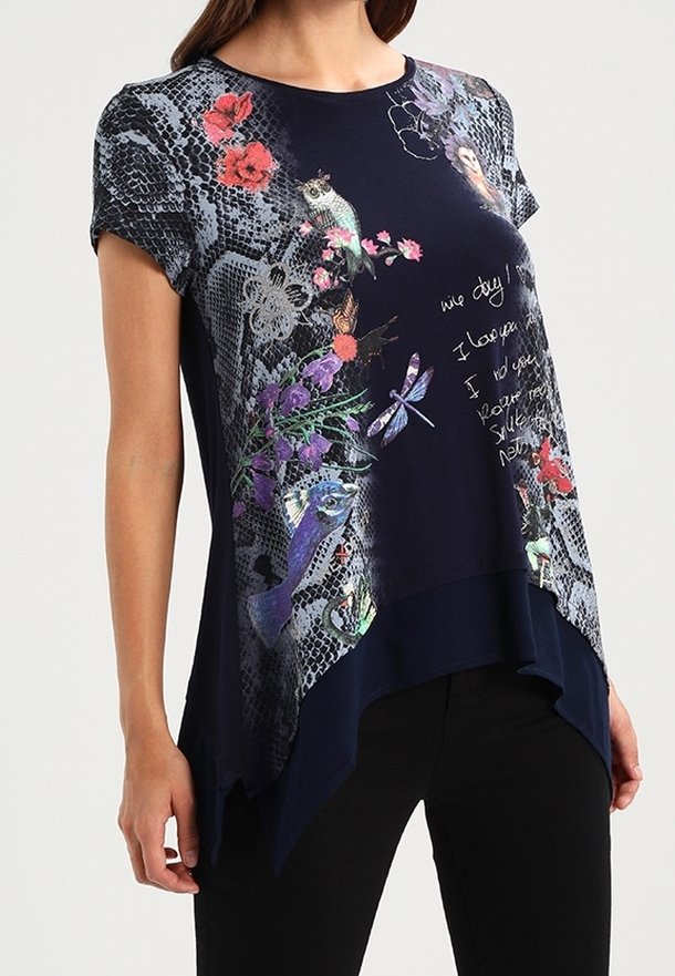 Marinblus med asymmetrisk design, tryck av blommor, fåglar och trollsländor, spetsmönster och vit handskriven text, bärs med svarta byxor.