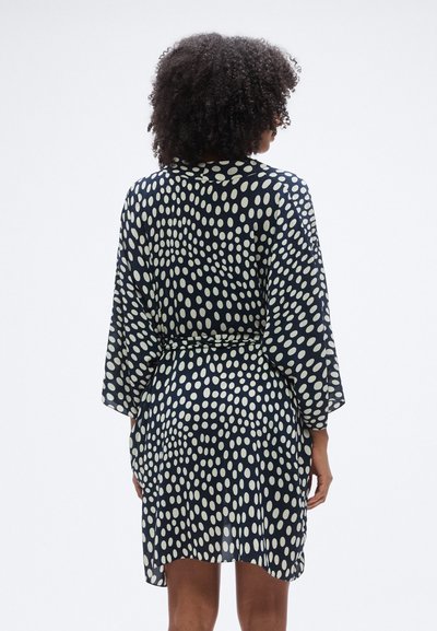 Μπλε ναυτικό ρόμπα με πουά μοτίβο σε κρεμ απόχρωση. Διαθέτει γιακά, μακριά μανίκια και ζώνη στη μέση. Ελαφρύ, απαλό ύφασμα.